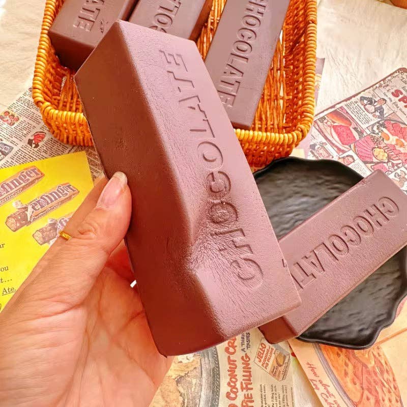 Hand holding a bar of chocolate with 'Chocolate' branding, surrounded by more chocolate bars and packaging.