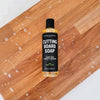 Bottle of cutting board soap on a wooden surface with soap suds.