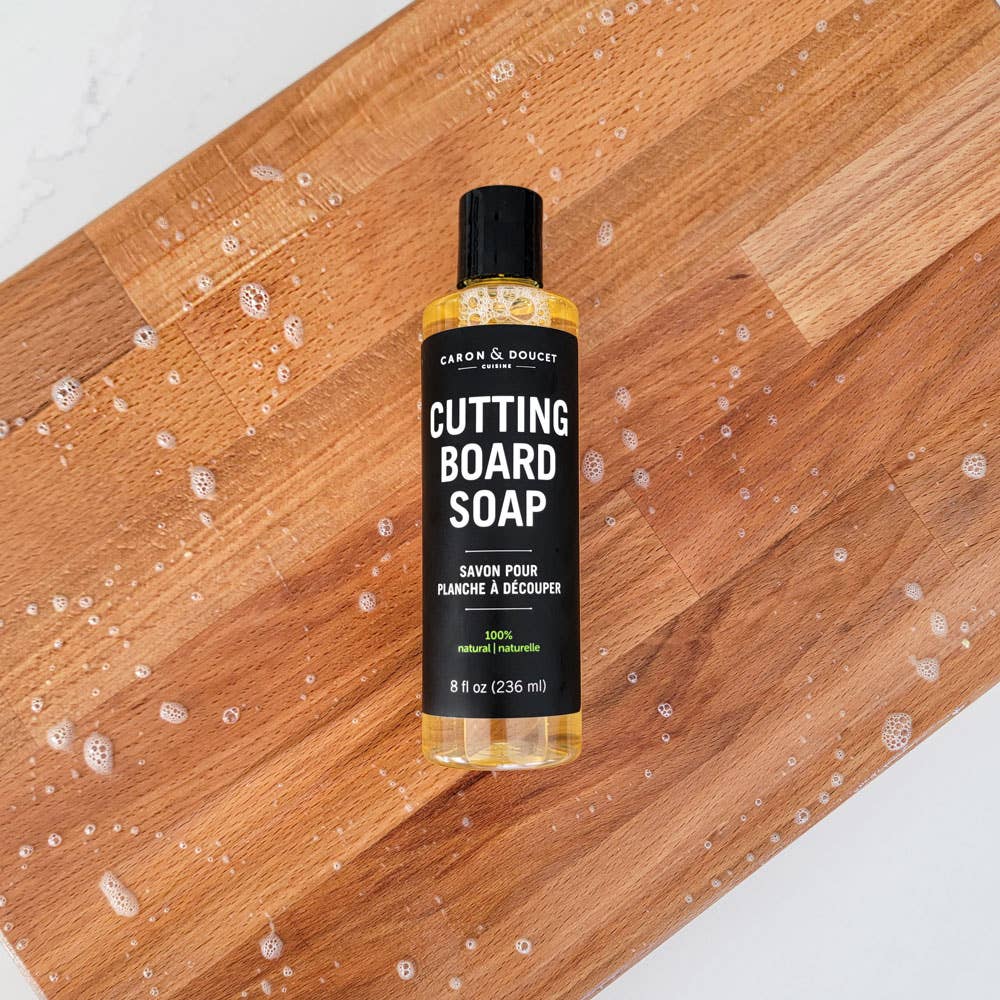 Bottle of cutting board soap on a wooden surface with soap suds.