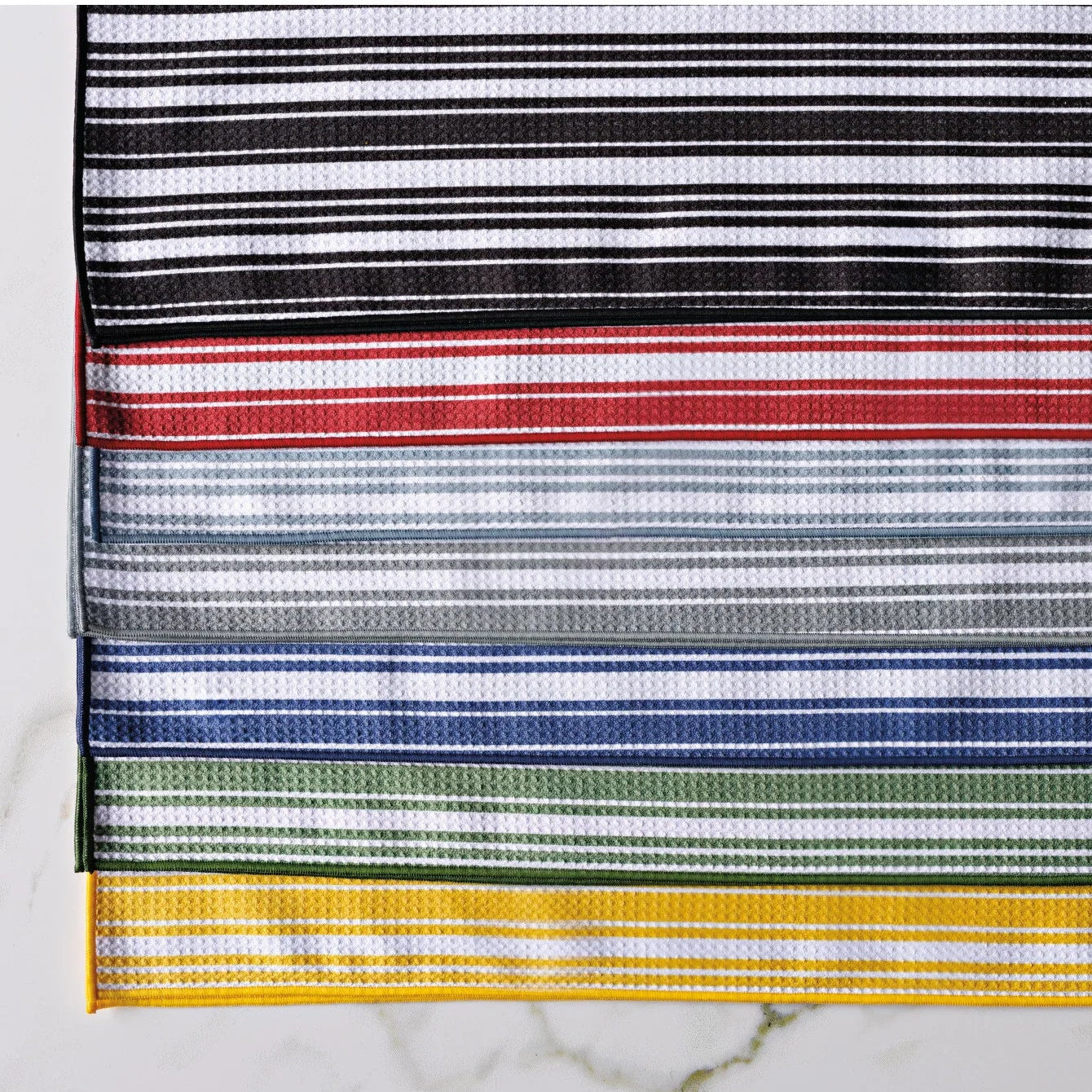 Striped kitchen towels available in black, red, blue, green, and yellow on a white marble background