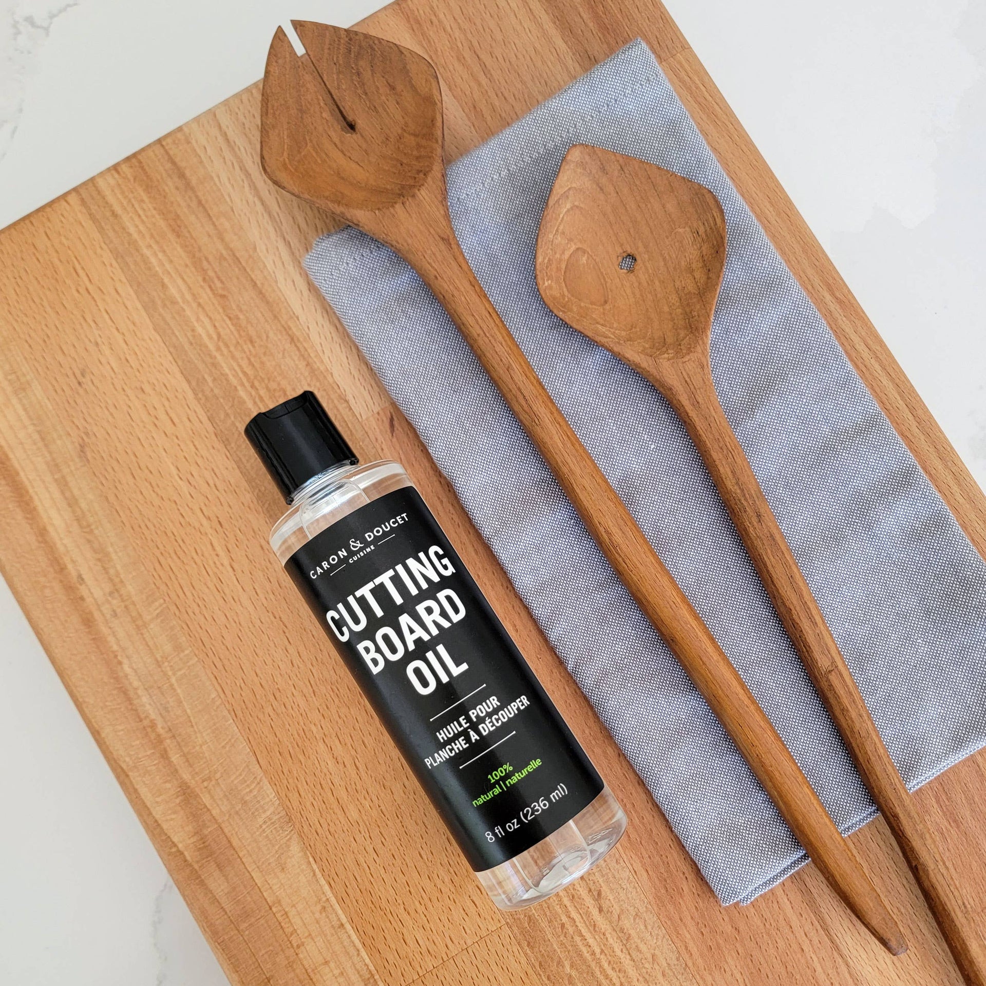 Bottle of cutting board oil on a wooden cutting board with wooden spoons and a cloth.