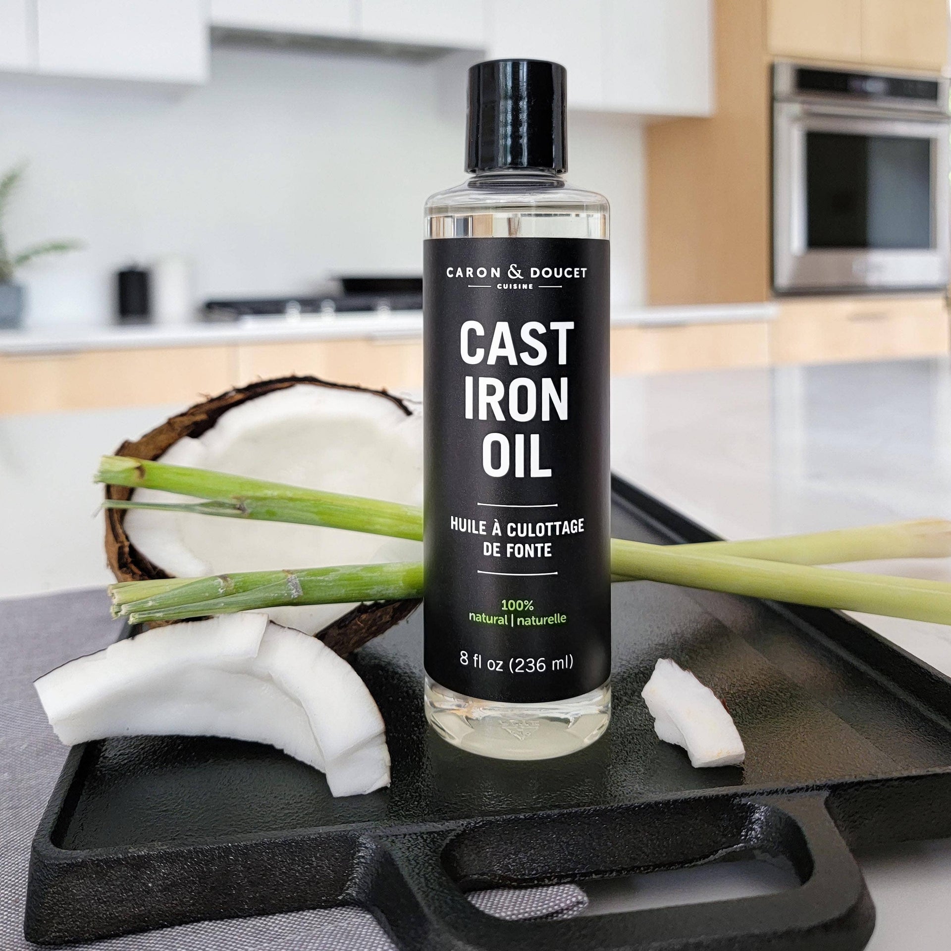 Bottle of Cast Iron Oil by Caron & Doucet on a kitchen counter with a coconut and greenery.