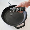 Person applying cast iron oil to a black cast iron skillet on a light background