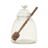Clear glass jar shaped like a beehive with a wooden honey dipper on a white background