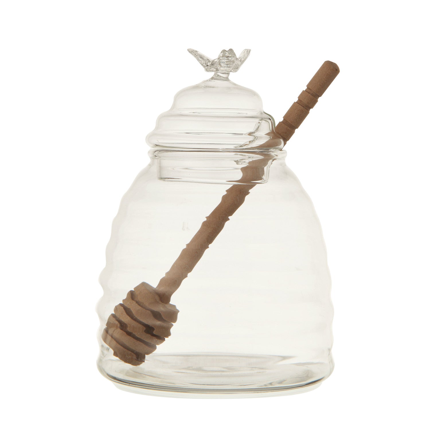 Clear glass jar shaped like a beehive with a wooden honey dipper on a white background