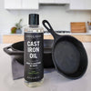 Bottle of Caron & Doucet Cast Iron Oil with a black cast iron skillet on a kitchen counter.
