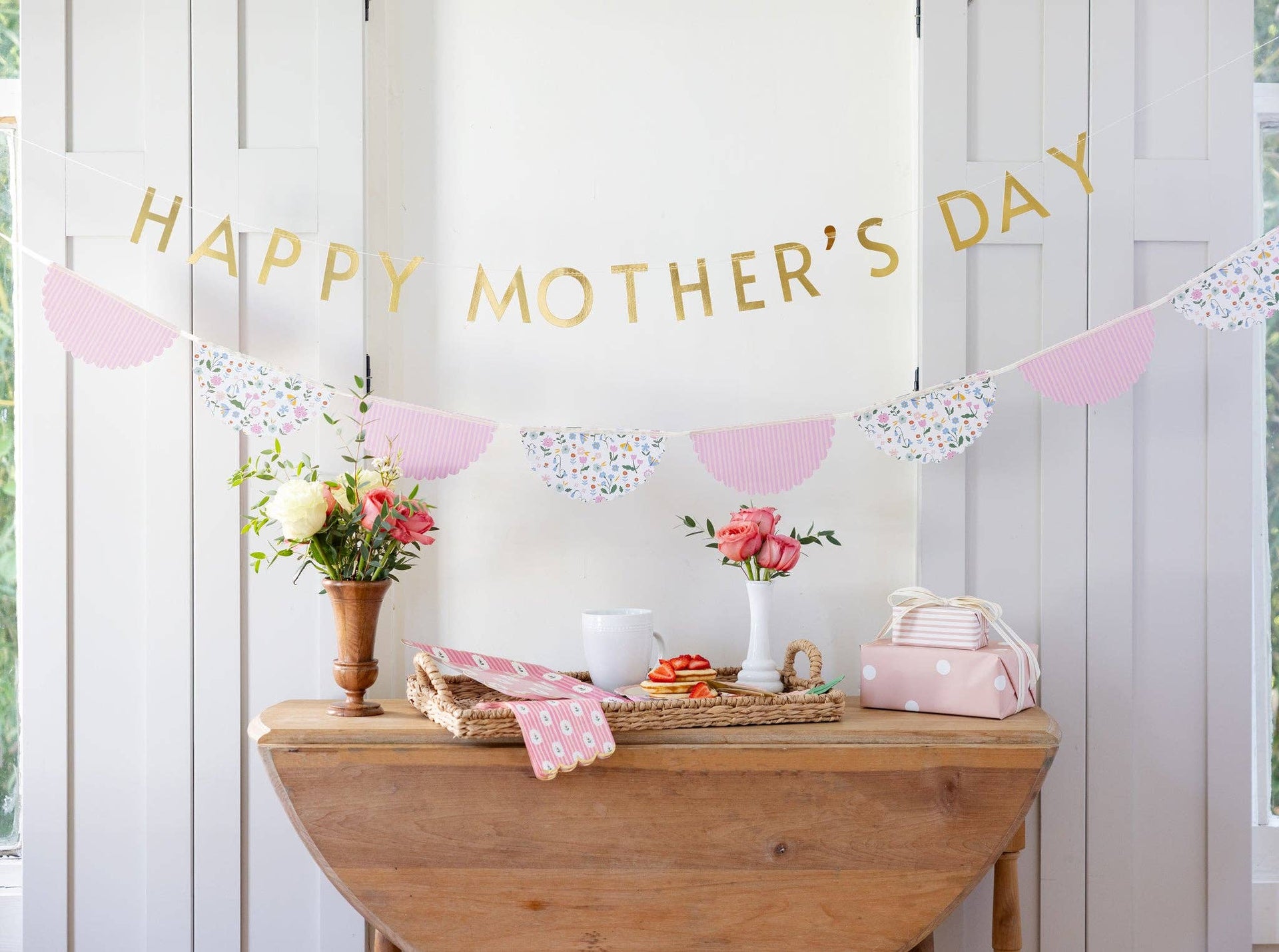 Decorative setup with 'Happy Mother's Day' banner, flowers, and a wooden table.