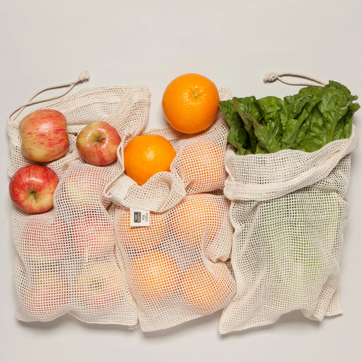 Mesh produce bags filled with fruits and vegetables on a white background