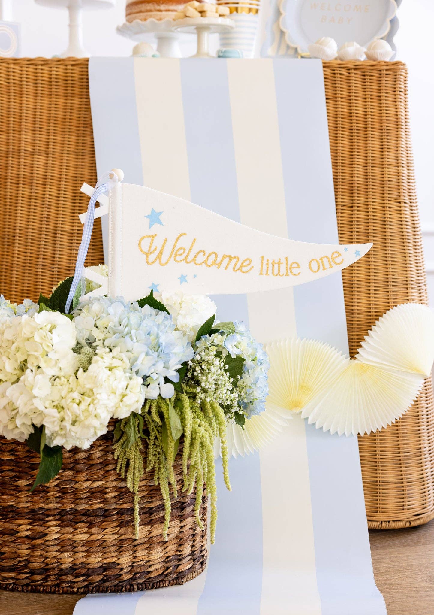 Decorative setup with flowers, a basket, and a 'Welcome little one' sign on a white background.