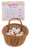 Wicker basket with cake charms and a 'Celebrate!' card on a white background
