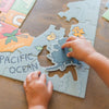 Child's hands playing with a puzzle of a world map on a wooden surface