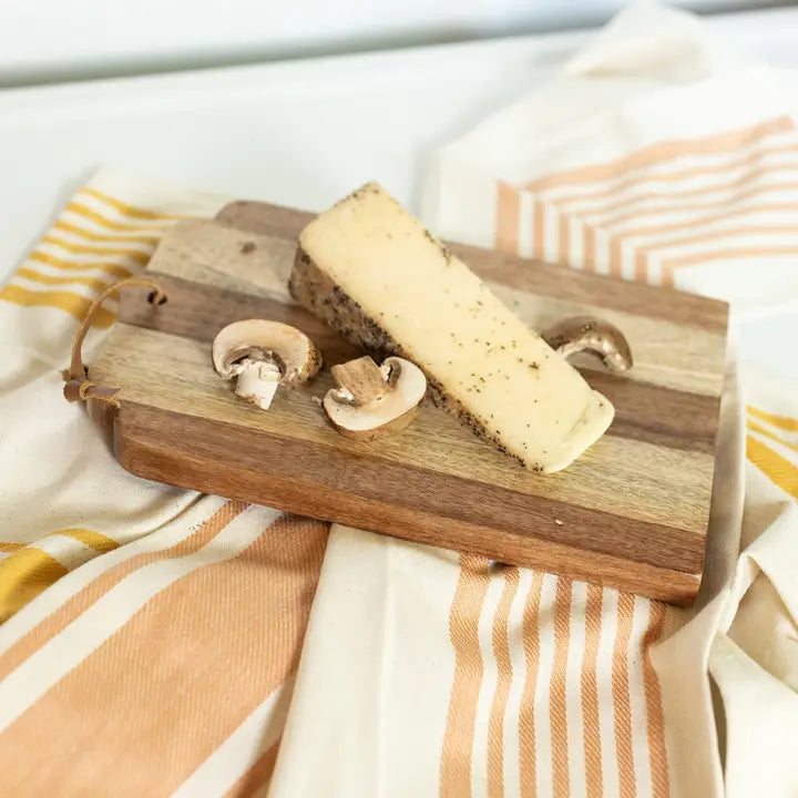 Cheese and mushrooms on a wooden cheese board with a striped cloth background