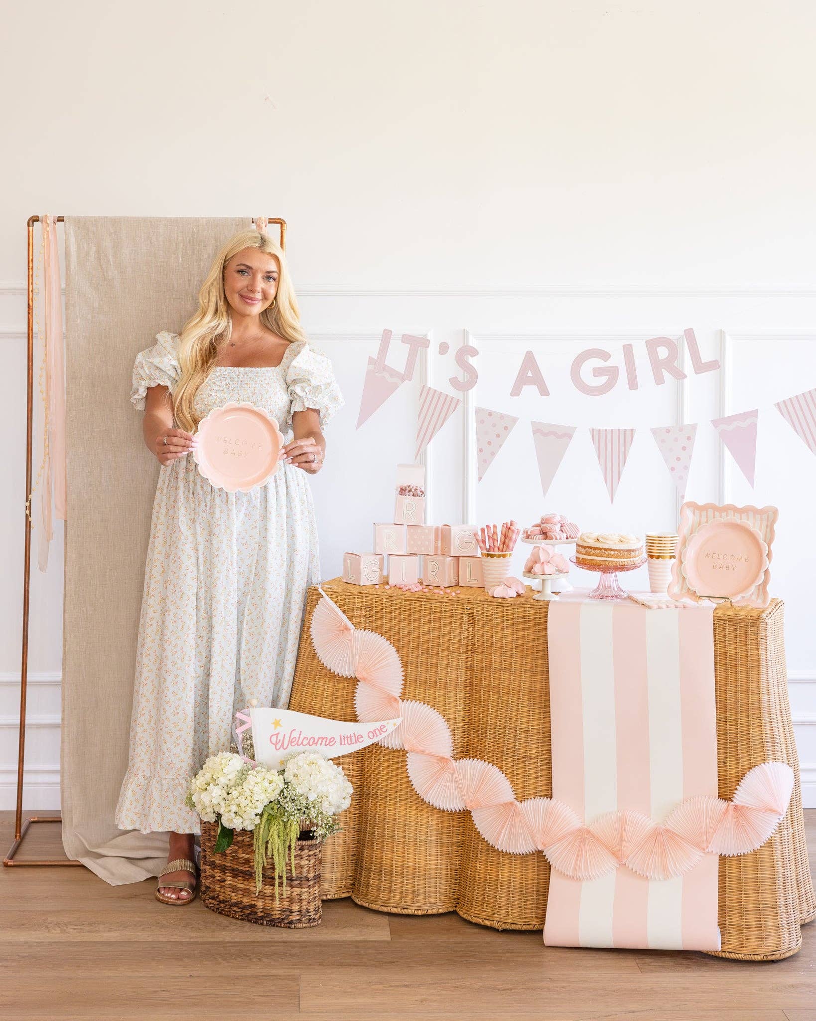 Woman in a long dress holding a pink plate next to a decorated table with 'It's a Girl' banner.