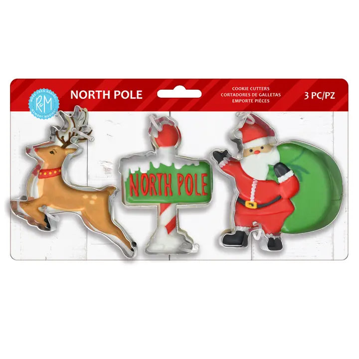 A 3-piece Christmas cookie cutter set in retail packaging, featuring a reindeer, a candy cane with a 'North Pole' sign, and Santa Claus with a green sack.