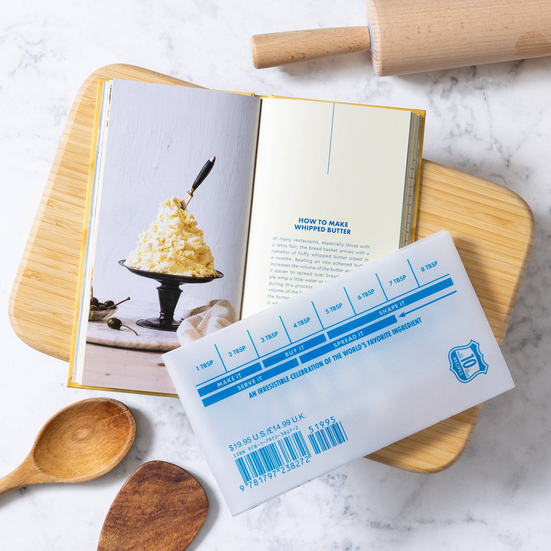 Butter book with measurement scale on open to a recipe for whipped butter, surrounded by wooden spoons and a rolling pin.