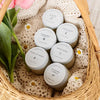 Assorted small jars with lids in a woven basket with flowers and doilies.