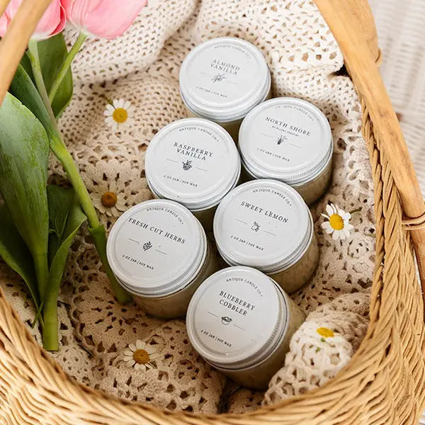 Assorted small jars with lids in a woven basket with flowers and doilies.