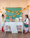 Two children in a classroom setting with a green chalkboard and decorative elements.