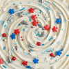 Close-up of a cake with white frosting, red, blue, and silver sprinkles.