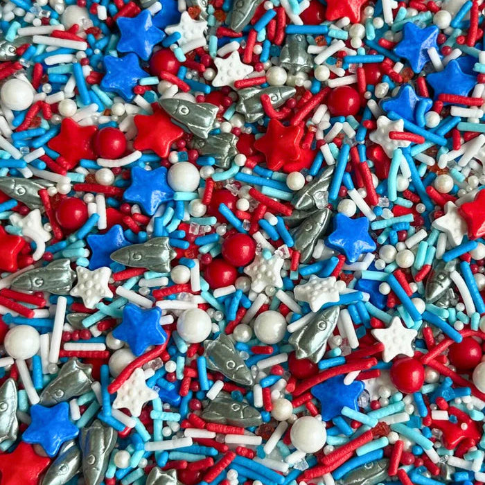 Colorful patriotic-themed sprinkles with stars, rocket ships and other shapes, in red, white, blue and silver.