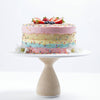 Colorful layered cake with sprinkles on a white and wood cake stand against a white background
