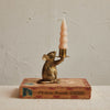 Bronze mouse candle holder with a candle on an old book against a textured wall.