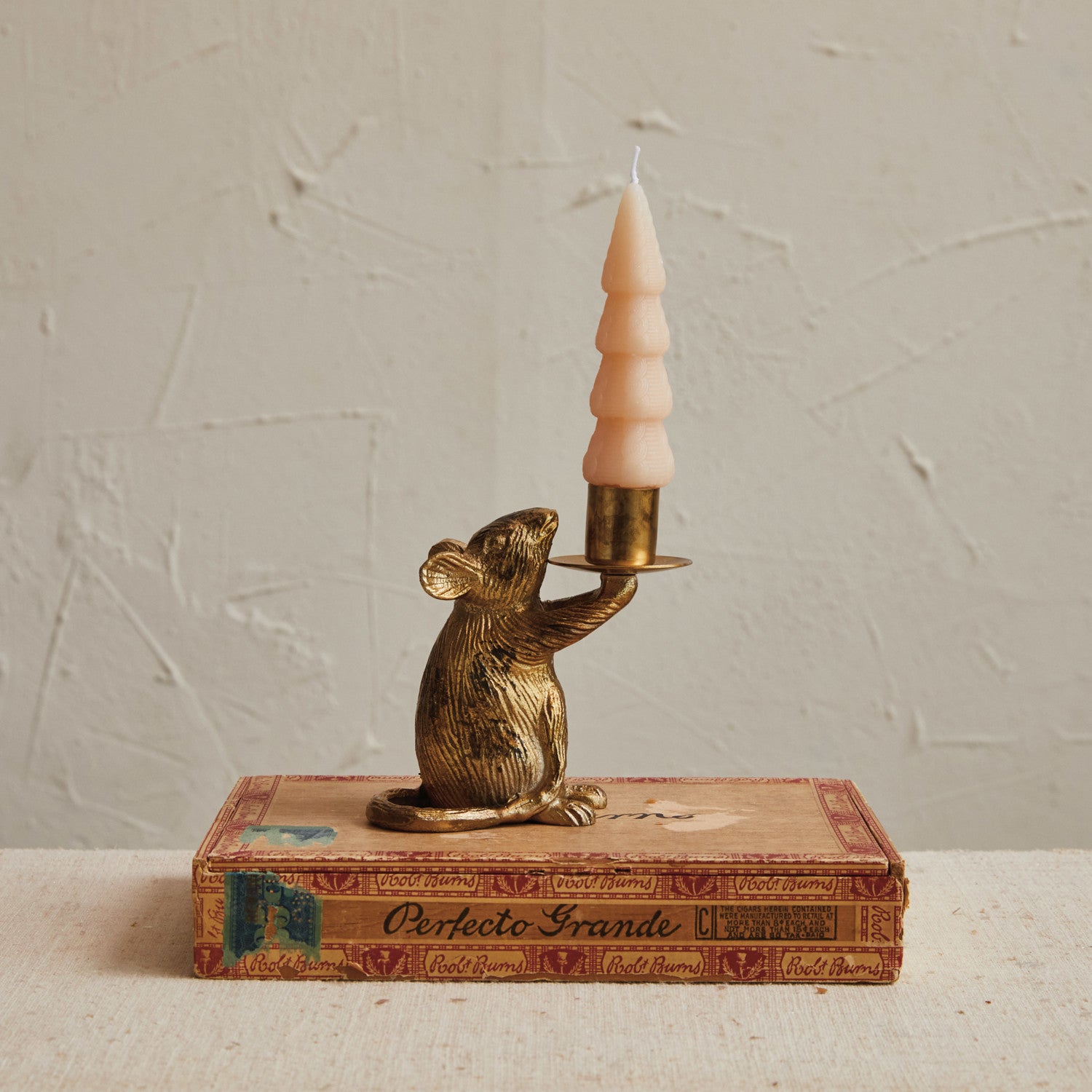 Bronze mouse candle holder with a candle on an old book against a textured wall.