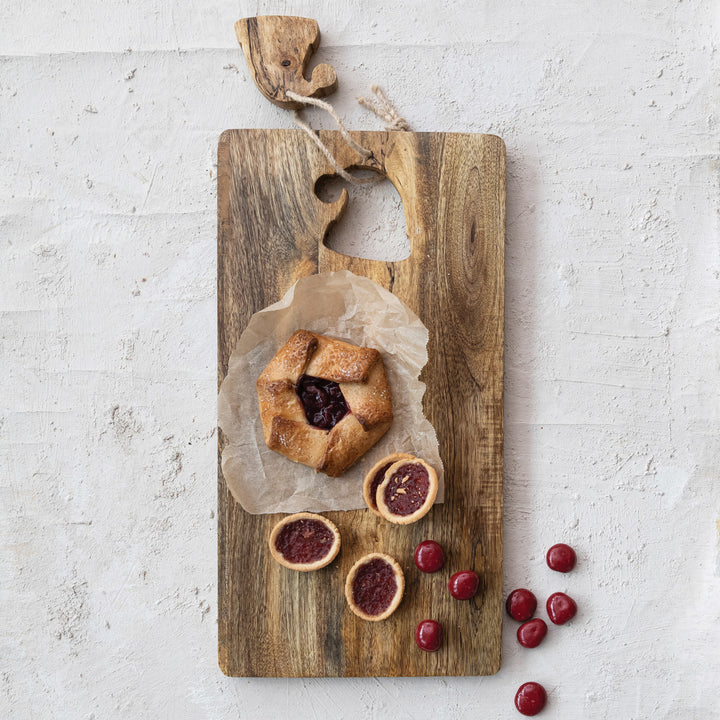 Wooden cheese board with Santa hat cutout design with a galette and cherry tarts on a light gray background 