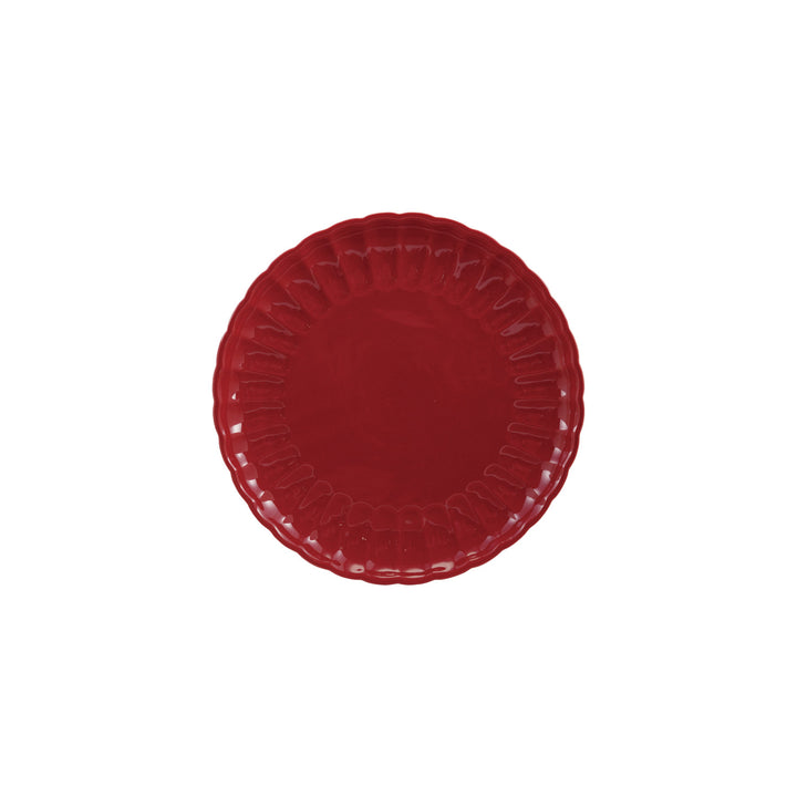 Red stoneware plate with scalloped edge on a white background